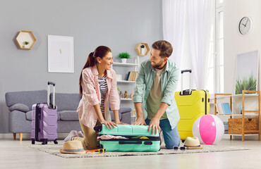 Naklejka premium Positive couple getting ready for summer vacation, travel or journey, packing their suitcase together at home. This family trip preparation showcases holiday excitement and togetherness.