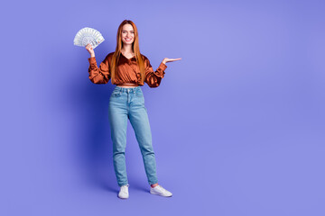 Full size photo of pretty young woman hold cash empty space wear brown shirt isolated on violet...