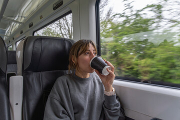 Traveling by public transport, woman drinks coffee from a recyclable cup while admiring the...