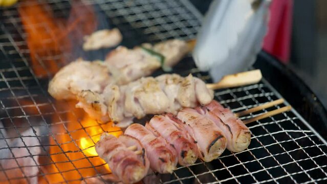 Grilling a pork barbeque skewers in a camping charcoal grill. Hand flipped a raw barbeque meats