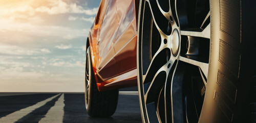 Close-up side view of an orange luxury sports car on the road as the sun sets.