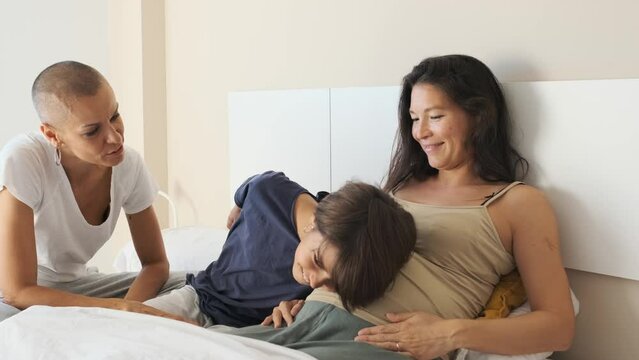 Non-binary child listening to pregnant mother's belly in bed