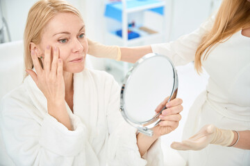 Female client checking the state of her skin after lifting procedure