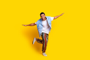 Full length photo of good mood ecstatic guy dressed jeans waistcoat print pants hold palms like wings isolated on yellow color background