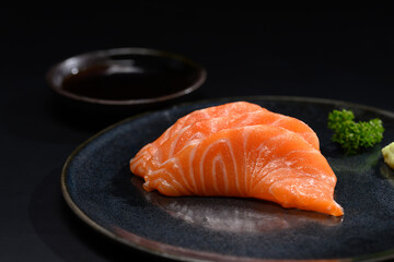 Close up sliced salmon sashimi serve on black plate with parsley leaf. Japanese food style