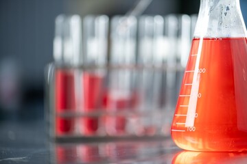 A close up of a wide-mouth graduated conical flask, three-quarters full with a transparent red...