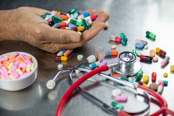 A pile of pills in the palm of an elderly person's hand with a stethoscope lying nearby.