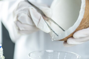 A gloved hand holding a pair of tweezers is extracting a sample from a coconut.