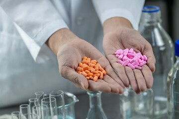 A scientist wearing a lab coat holds two handfuls of pills in their hands.