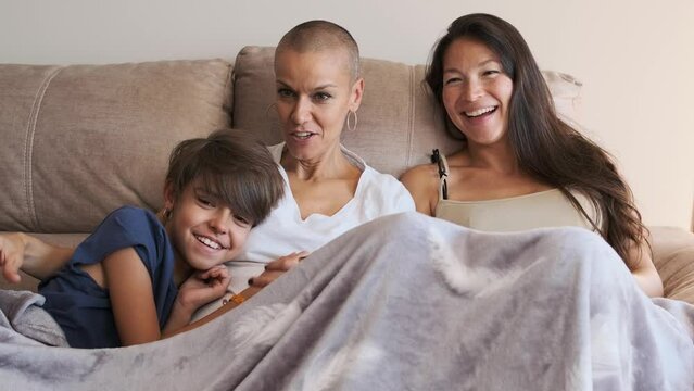 Relaxed lesbian pregnant couple with a child on the sofa watching television