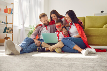 Happy mum, dad and kids dressed in red capes relaxing on holiday weekend, sitting on floor rug with...