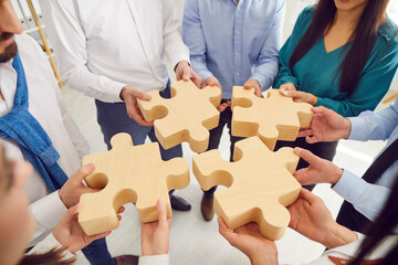 Top view hands of a group of business people assembling big wooden puzzle. Coworkers join jigsaw...