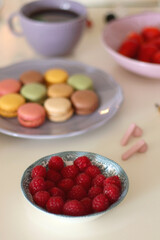 Plate of pastel macarons, cookies and chocolate, cup of tea of coffee, glass of bubble water, various berries, books and accessories on the table. Selective focus, pastel colors.