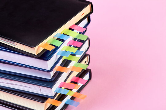 Close-up of a stack of office notepads with colorful sticky page markers sandwiched between pages on pink background