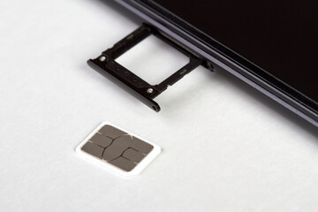 SIM card near the smartphone with an open sim card tray on light background
