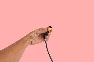Black male hand holding a MIDI audio cable isolated on pink background