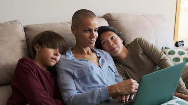 Lesbian pregnant couple with a child on the sofa watching a movie with a laptop