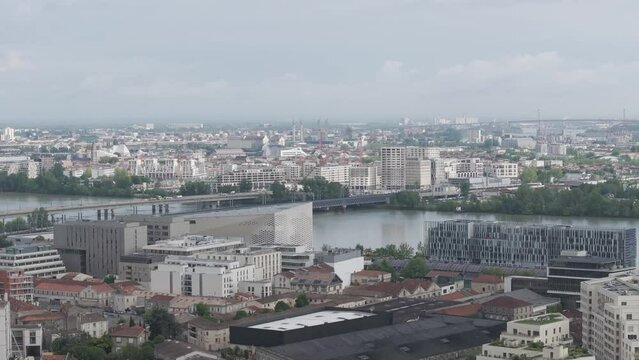 The Meca cultural center and  high-speed train arriving at station over Passerelle Eiffel bridge crossing the Garonne River in Bordeaux France, Aerial rising reveal shot