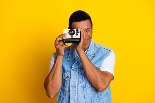 Photo of optimistic guy dressed jeans waistcoat holding retro camera on eye make photo isolated on vibrant yellow color background