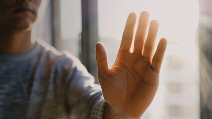 A person offering a gesture of peace or stopping with an outstretched hand in a soft, sunlit setting.