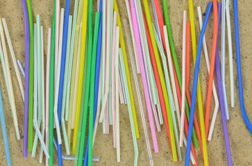 Colorful plastic straws on a sand, beach after summer party. Trash.  Top view.