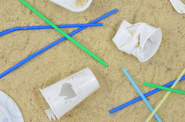 White plastic cups and plates, colorful, plastic straws on the beach. Dirty sand after summer party, summer vacations or festival. Say no to plastic.