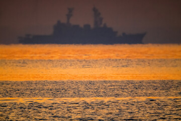 朝焼けが波間に映える海で沖に護衛艦の船影20220604-1