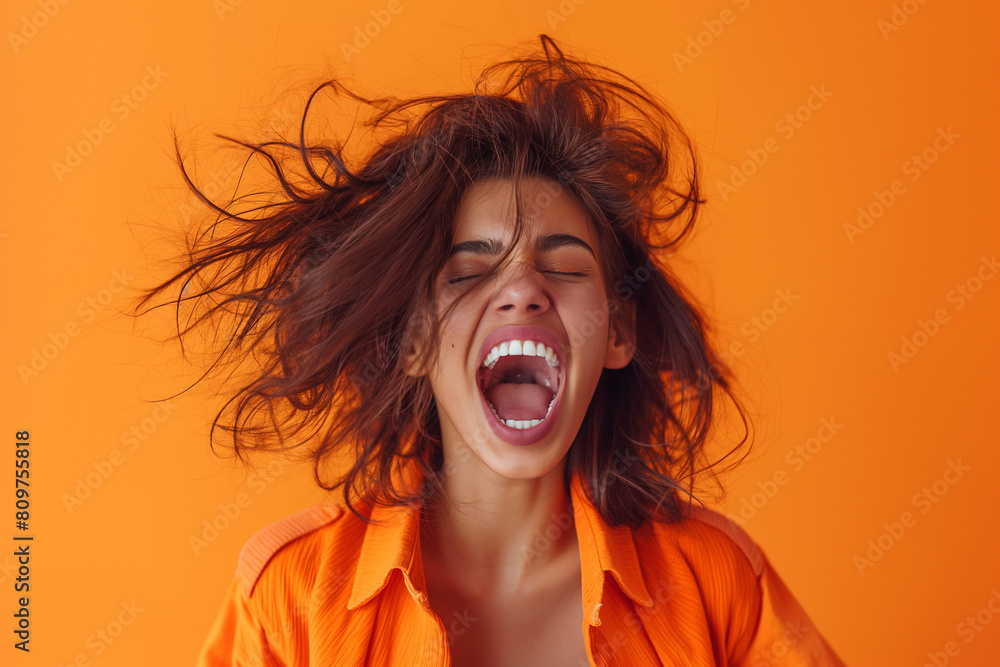 Wall mural portrait of an excited woman with an open mouth and messy hair screaming, isolated on an orange back