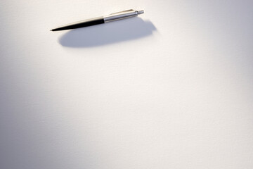 A sleek silver and black pen rests on an untouched white sheet, implying preparation for writing.