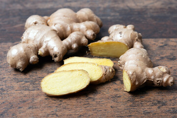 Fresh ginger root with cut slices on wooden background, close up,