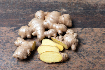 Fresh ginger root with cut slices on wooden background, top view