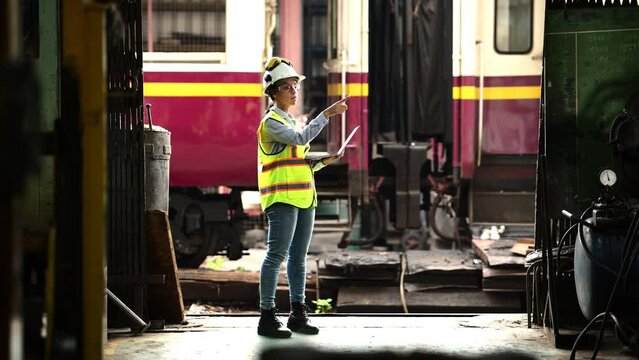 Portrait of railway technician worker in safety vest and helmet working with tablet at train repair station