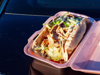 Chicken kebab wrap meal in a plastic pink container on blue car trunk. Take away food with high...