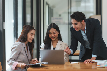 Group of young Asian business people brainstorming, looking at laptop computer.