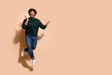 Full length portrait of nice young man jump point fingers empty space wear sweater isolated on beige color background