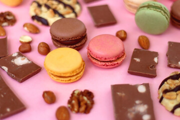 Pastel macarons, almond chocolate, peanut butter cookies and various nuts on bright pink background. Selective focus.