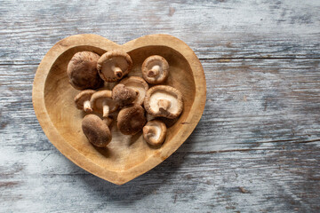 Raw shiitake mushrooms in a heart shaped wooden bowl
