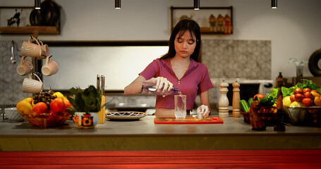 Indian Asian Hindu thirsty tired teen girl child standing modern home kitchen hold bottle pouring purifier natural drink water glass gen z cute young adult lady female fresh indoor house spend time