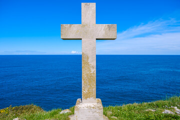 A Christian cross stands tall on a hill, casting a shadow against the backdrop of the vast ocean with waves crashing below. The scene exudes a sense of solemnity and reverence.