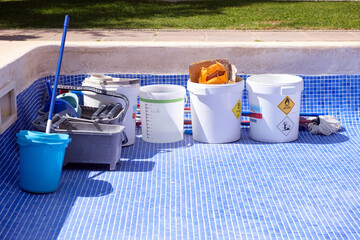 Multiple buckets filled with food placed on a blue tiled pool undergoing repair and sealing work.