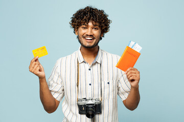 Traveler Indian man wear white casual clothes hold passport ticket, credit, bank card isolated on plain blue background. Tourist travel abroad in free spare time rest getaway. Air flight trip concept.