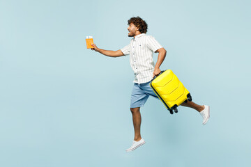 Full body traveler Indian man in white casual clothes hold passport ticket bag jump high run isolated on plain blue background Tourist travel abroad in free time rest getaway Air flight trip concept