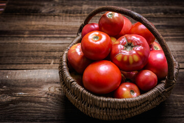 Basket of fresh natural tomatoes on wooden background.