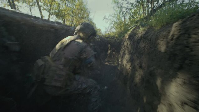 Ukrainian soldier or military man in camouflage uniform and helmet runs in trench and shoots from automatic rifle during assault and attack on enemy positions. War or military conflict. Armed forces.