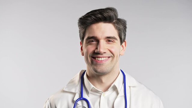 Handsome doctor man winking eye, smiling to camera. Guy in studio on white