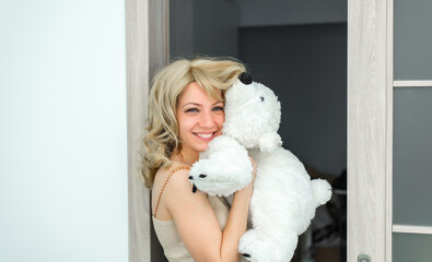 A beautiful girl is holding a white toy, possibly a polar bear. She smiles and she is happy.