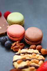 Macarons, chocolate, cookies, berries and various nuts on dark blue background. Selective focus.