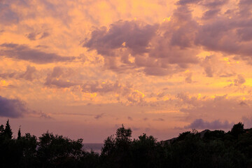 Colourful sunset in the bay of Agios Georgios with dark clouds in front of an intensely orange sky with individual strangely shaped dark wispy clouds on the island of Corfu