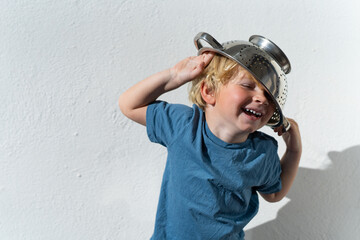 Little boy putting colander on his head . cheerful blond boy with a sieve on his head. positive kid