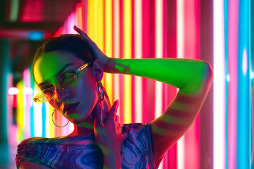 Glamour in neon illumination. Striking portrait of woman wearing stylish sunglasses that reflect...